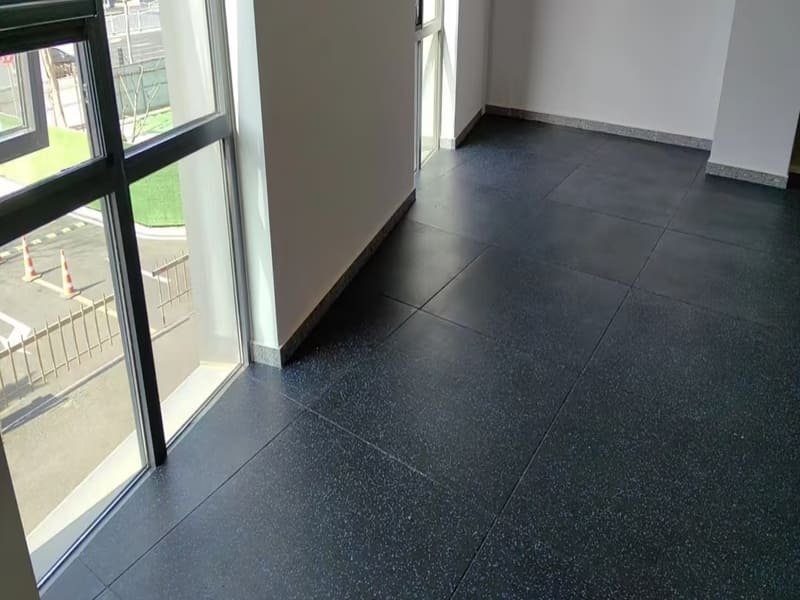 Duas pessoas desenrolam cuidadosamente um pesado rolo de pavimento de borracha numa garagem.